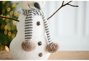 Detail of plush Christmas snowman with striped scarf and bronze bell buttons on wood