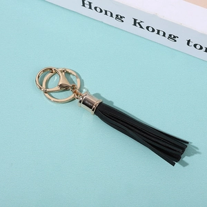 Close-up of black PU tassel keychain with golden metal ring and lobster clasp on teal background