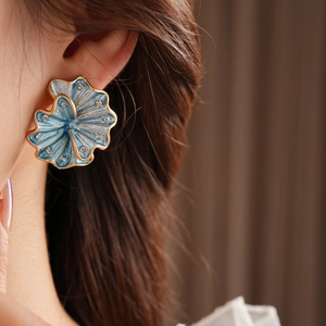 Close-up of blue flower stud earrings with gold edges and diamonds worn by a model