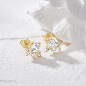 Detail of gold cat paw earrings with clear zircon on a textured white stone surface