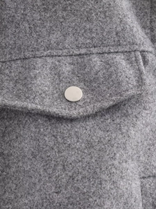 Detail of grey faux fur jacket showing pocket flap and polished metal snap button