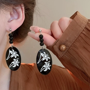 Macro view of vintage black earrings with white lily print and silver hooks on ear