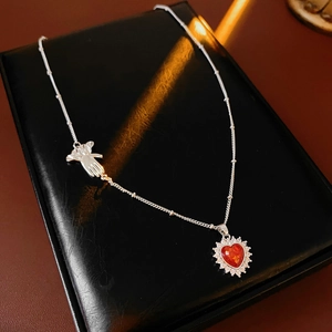 Macro shot of silver glove charm and red heart pendant with zircon on black leather