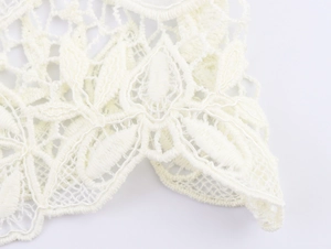 Detail shot of white lace stitching with floral embroidery on a knit top sweater