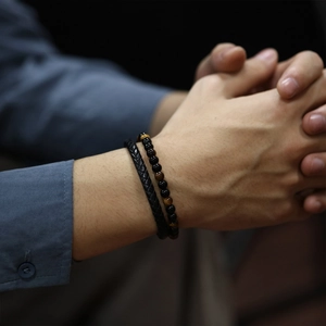 Close-up of men's black braided leather and red tiger eye stone beaded bracelet set on wrist