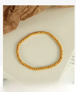 Detail view of polished gold bead bracelet for women on a textured white surface