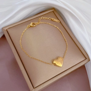 Detail of a minimalist gold heart pendant on a titanium steel chain bracelet