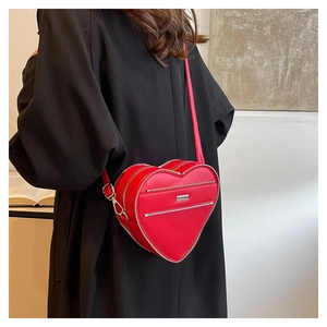Detail of red heart-shaped crossbody bag with decorative zippers on black dress