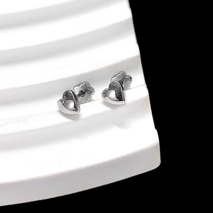 Detail of silver heart-shaped stud earrings on a white minimalist display stand