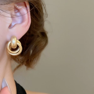 Macro shot of triple-layered interlocking matte gold geometric hoop earrings on ear