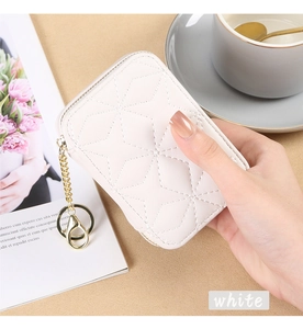 Close-up of white quilted mini pouch with gold zipper and keychain held by hand