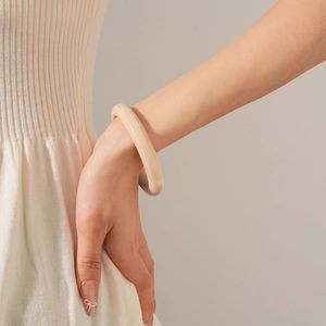 Close-up of a minimalist cream resin bangle worn on wrist with beige knit clothing