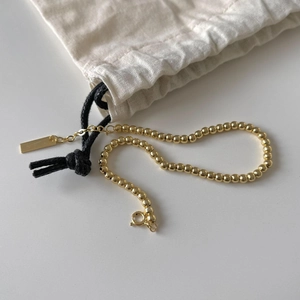 Detailed close-up of a minimalist golden bead bracelet on a white surface with a fabric pouch