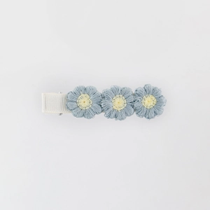 Detail of three light blue embroidered flowers on a white ribbon-wrapped metal hair clip