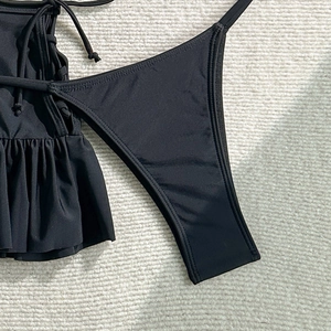 Detail view of black bikini set featuring ruffled trim and high-cut leg on beige fabric