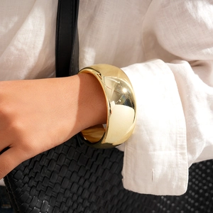 Close-up of wide polished gold bangle worn by model with textured fashion accessories