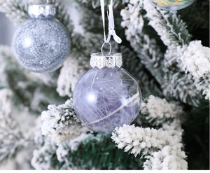 Macro shot of a transparent Christmas ornament with purple feathers on a snowy tree