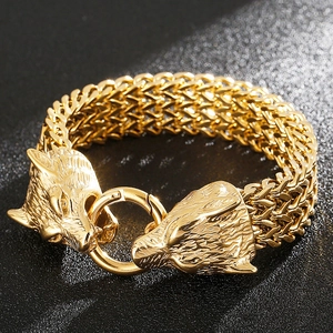 Macro detail of golden metal bracelet featuring double wolf head clasps on black surface