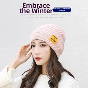 Close-up of pink ribbed knit beanie featuring a yellow 'MOMENT OF AMBITIONS' woven label