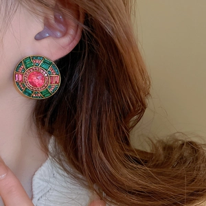 Close-up of vintage gold earrings with pink and green stones worn by a model