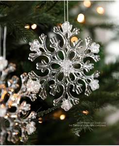 Macro view of transparent acrylic snowflake ornament with white glitter on a festive tree