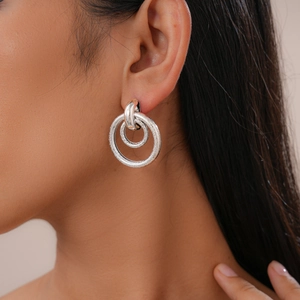 Close-up of geometric matte silver double hoop earrings worn by a model in detail