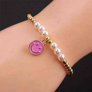 Gold-plated beaded bracelet featuring pink smiley face charm and white pearls on wrist