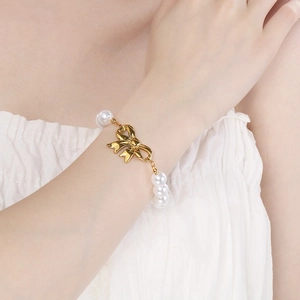 Detailansicht eines goldenen Schleifen-Perlenarmbands am Handgelenk im Sommerlicht