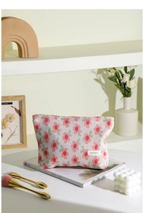 Close-up detail of knitted floral makeup bag with pink flower pattern and woven brand label