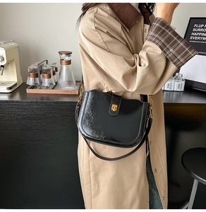 Detail of elegant black patent leather saddle bag featuring a gold square metallic clasp