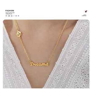 Dettaglio della collana dorata con ciondolo Dreams su tessuto di pizzo bianco