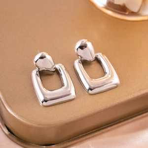 Macro shot of silver plated hollow rectangular earrings on a gold textured surface
