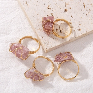 Detailed view of handmade wire-wrapped rose quartz rings on a textured stone surface