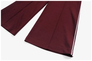 Close-up of deep red track pants featuring white side stripes and stitched front crease