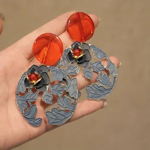 Detail of ethnic style earrings featuring red circular resin and blue enamel leaf charms