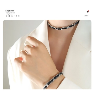 Détail d'un ensemble collier et bracelet en cuir tressé noir sur un blazer blanc