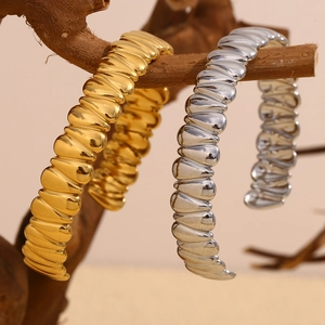 Detail of twisted metal bangle set in gold and silver hanging on a wooden branch