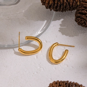 Close-up of minimalist gold-plated U-shaped stud earrings on a white textured surface