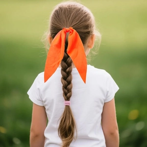 Detail of vibrant orange silk bow hair clip styled on braided hair with natural backdrop