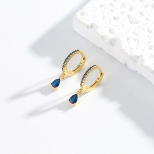 Detail of gold fan-shaped earrings with drop-cut blue crystals on textured stone