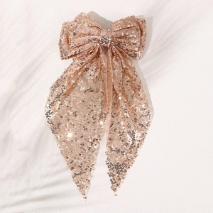 Close-up of champagne gold sequins on large bow hair clip with flowing ribbons