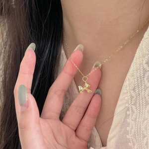 Macro shot of a delicate gold bow pendant necklace held by fingers on lace fabric