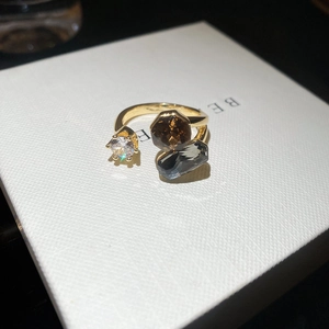 Detailed close-up of a gold geometric open ring with clear, amber, and grey crystals