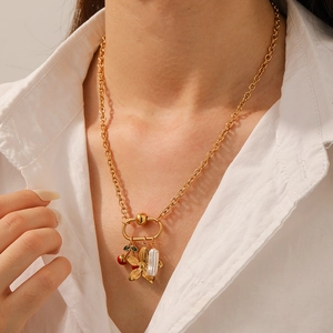 Close-up of gold cherry and pearl charms on a stainless steel necklace worn by a model
