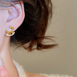 Close-up of golden rocking horse earrings with cubic zirconia worn by a model