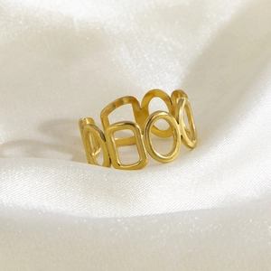 Macro shot of gold stainless steel cutout ring with square and round motifs on white silk