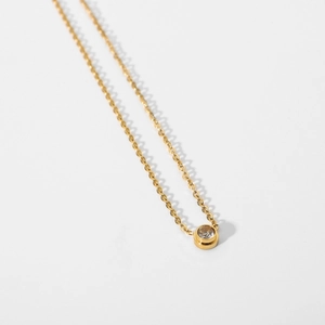 Macro view of a gold pendant necklace with a round bezel-set zircon on white background