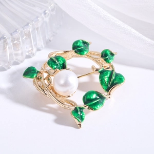 Detail of a gold vine brooch with green enamel leaves and a centered white pearl