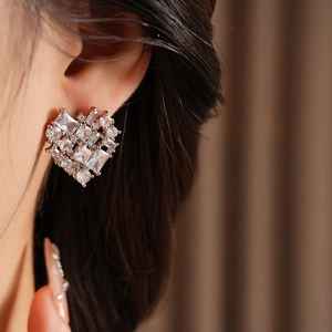 Close-up of heart-shaped silver earring with zircon and tiger eye stone inlay