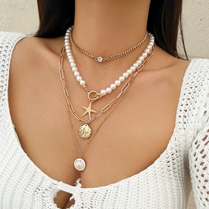 Detail of layered gold necklace featuring faux pearls starfish and shell pendants